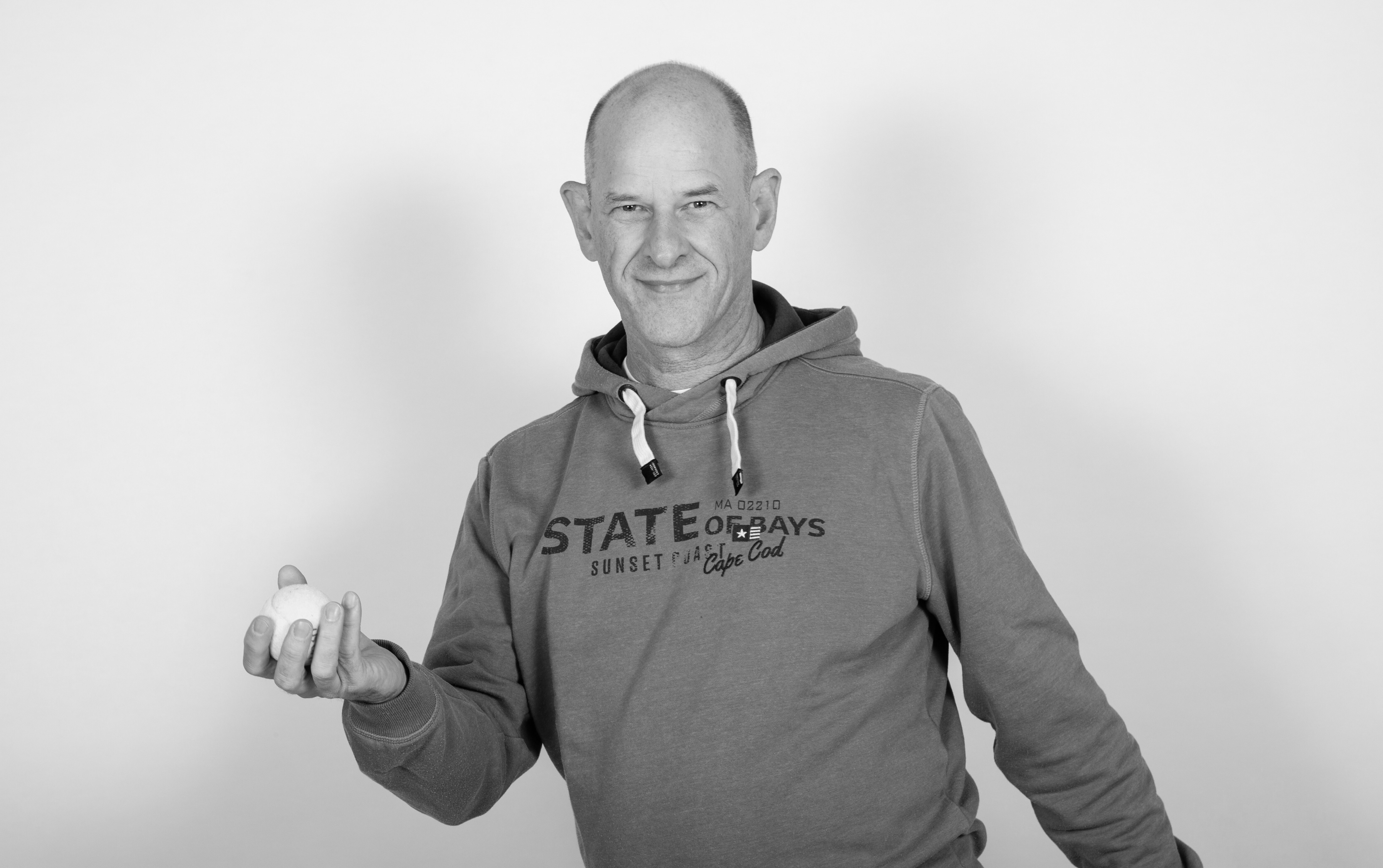 Sven Hemprich hält lächelnd einen Ball in der Hand, schwarzweißes Studiofoto
